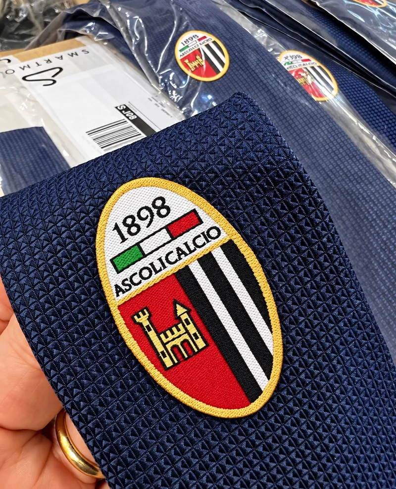 Cravatte blu con stemma Ascoli Calcio 1898, una in primo piano e altre nelle confezioni.