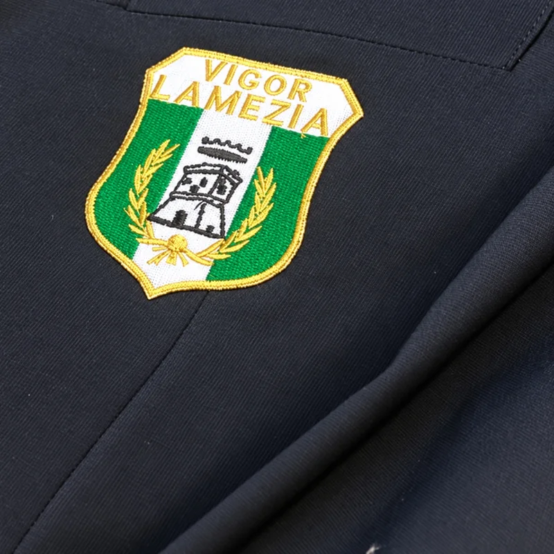 Dettaglio dello stemma verde, bianco e giallo della Vigor Lamezia su una giacca scura.
