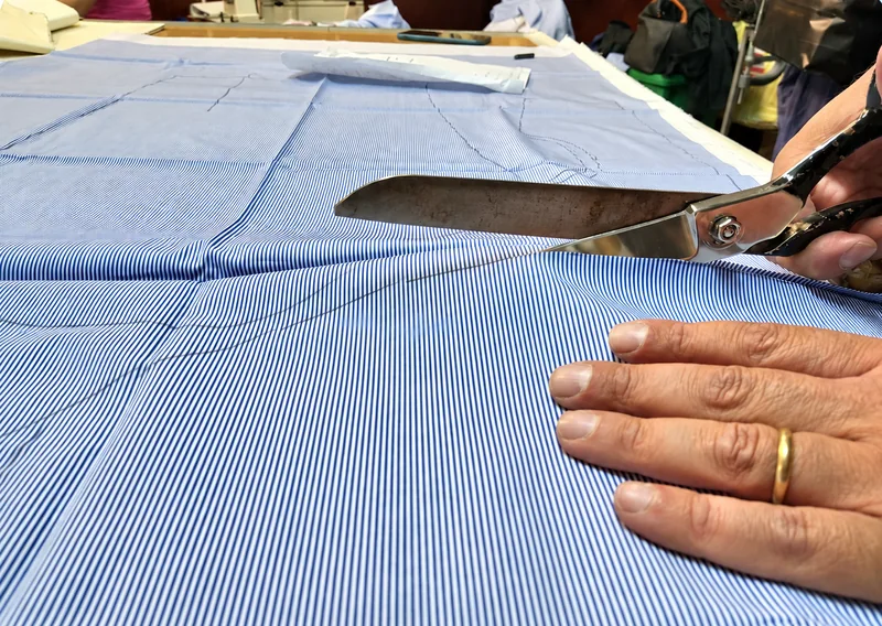 Le mani di Antonio Gigliotti tagliano il tessuto a righe con forbici sartoriali.