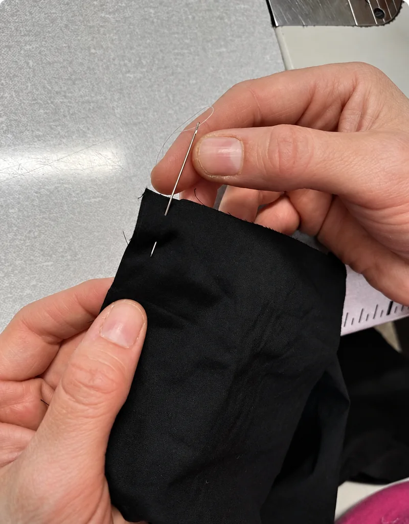 Cucitura manuale di un dettaglio del capo con ago e filo.