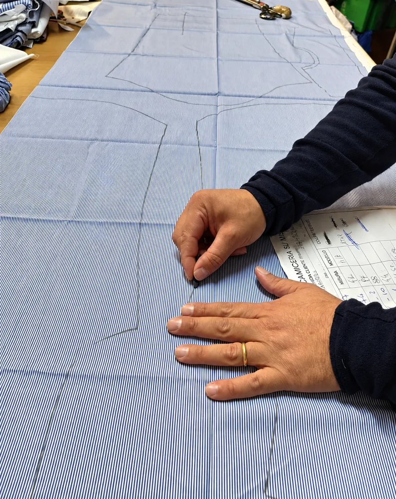 Le mani dell’artigiano tracciano il modello della camicia sul tessuto azzurro