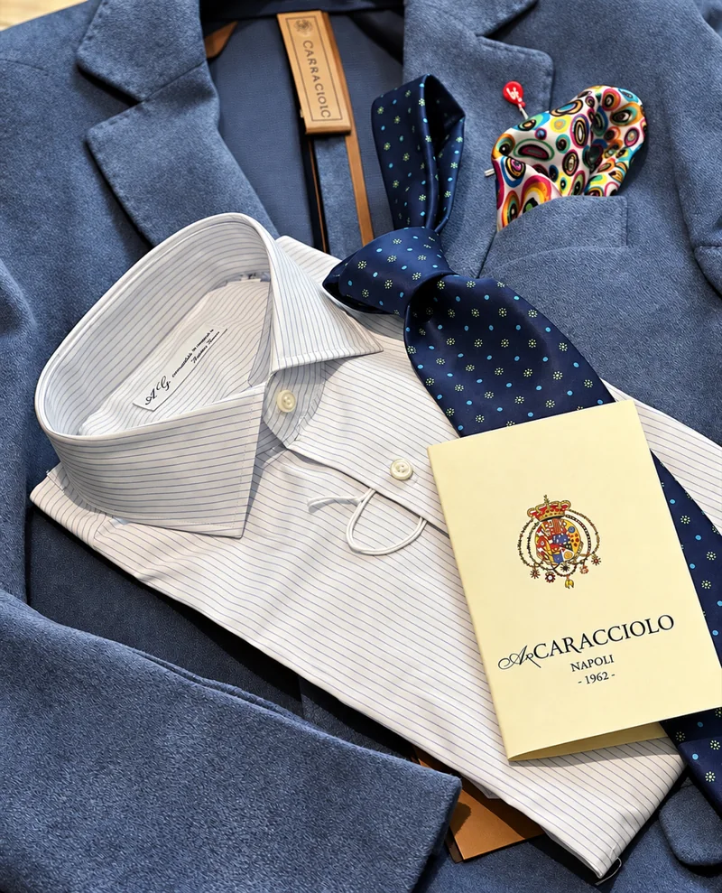 Giacca blu abbinata a una camicia a righe sottili, cravatta a pois e pochette colorata.