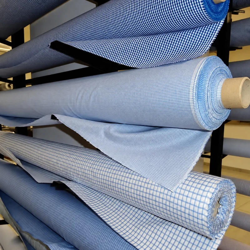 Rotoli di tessuto azzurro, blu e a piccoli quadri disposti su un espositore.