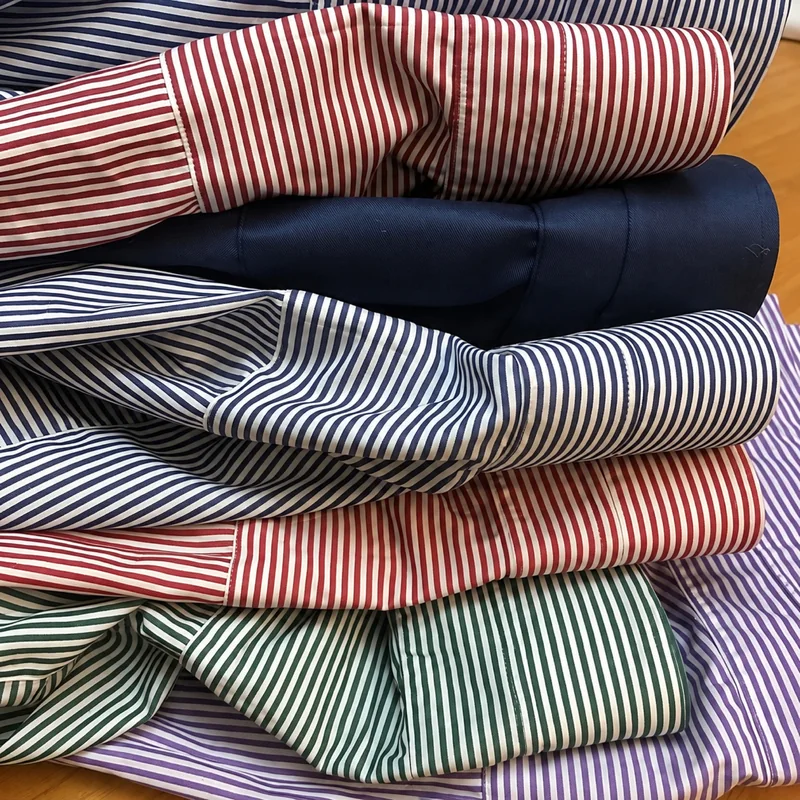 Tessuti per camicie a righe rosse, blu, verdi e viola, raccolti in pieghe.